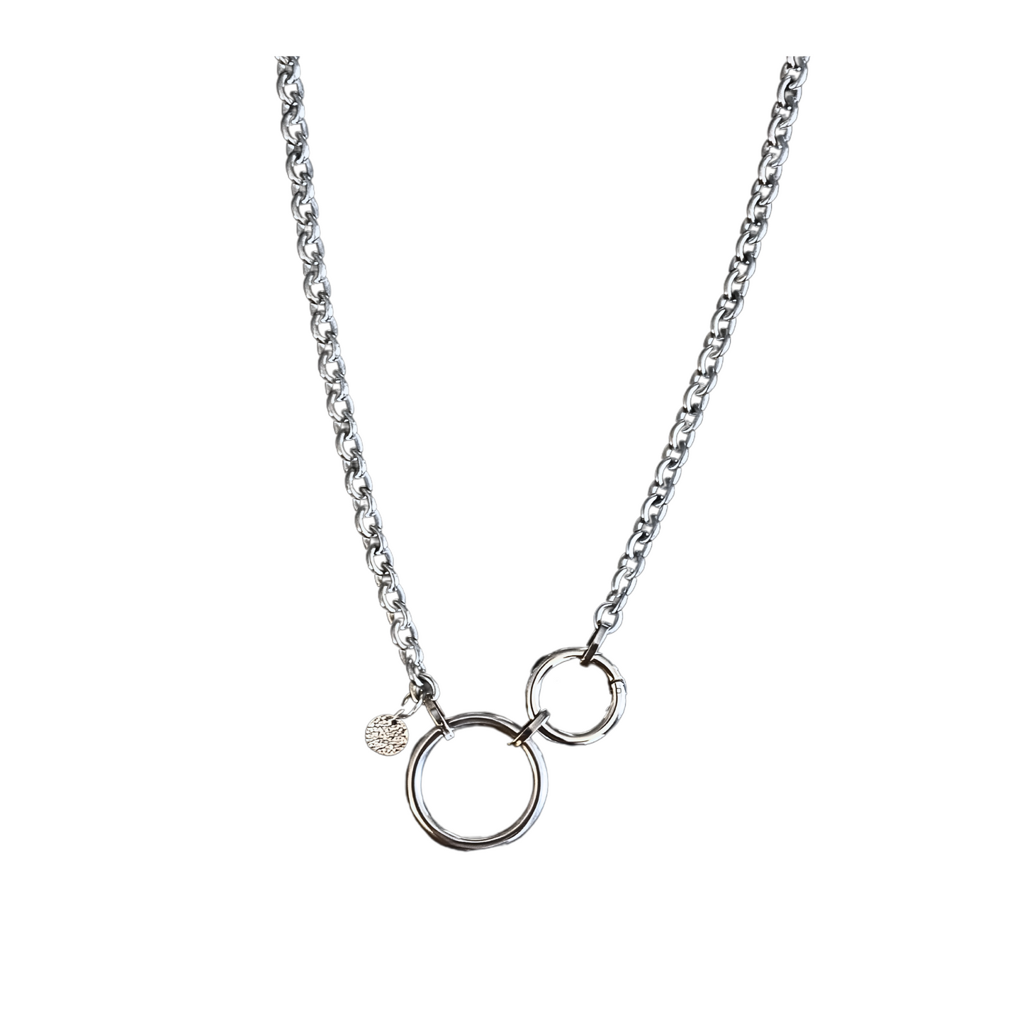 Stylishe Statementkette von Hug the Lioness Silber und Edelstahlschmuck. Die Halskette aus Edelstahl hat einen 32mm großen Ring aus Edelstahl und einen 24mm Ringverschluss. Die Kette ist vorne mit dem Ringverschluss zu verschließen. Als Detail ist ein 10mm gehämmertes Plättchen aus Sterlingsilber angebracht. Die Halskette ist 6mm breit und 55cm lang.
