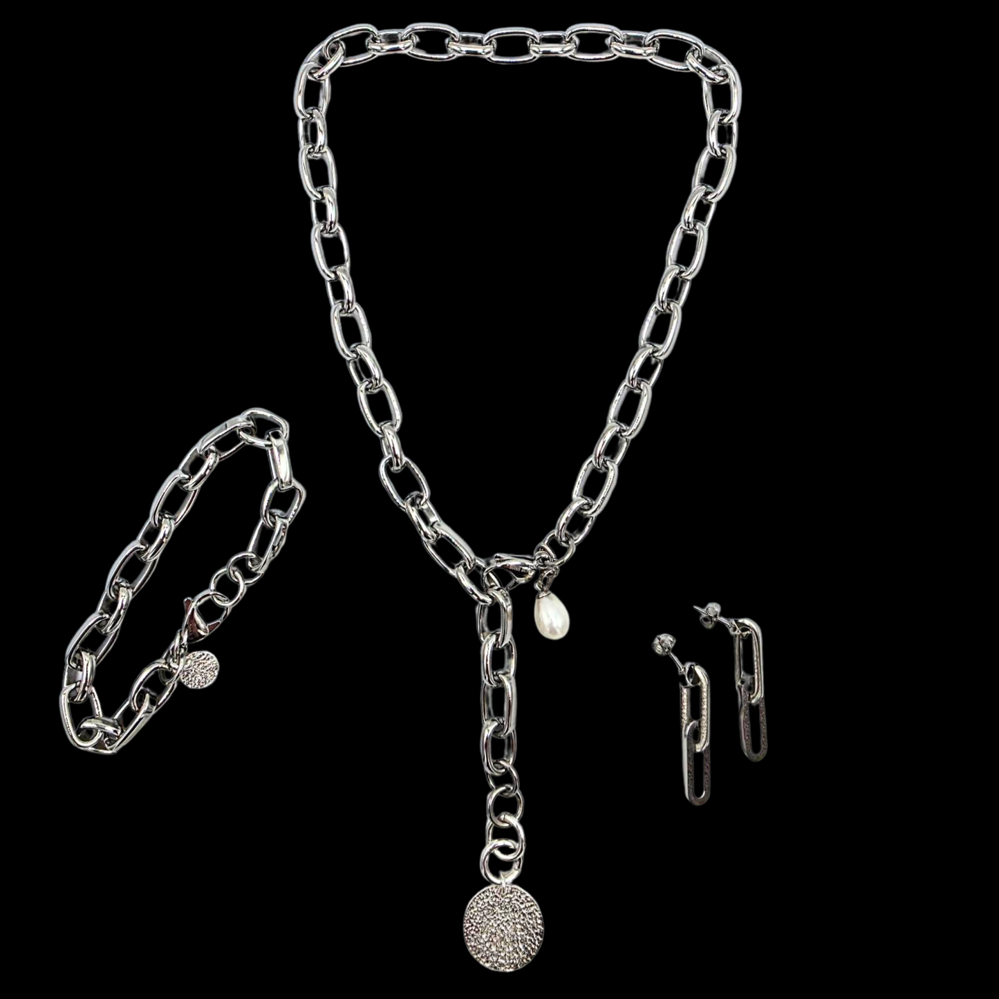 Exklusive silberne Y-Halskette 47cm aus 316L Edelstahl. Die Kettenglieder sind breit und glänzend. Die Halskette hat einen silbernen 20mm Anhänger aus gehämmerten Sterlingsilber in Form einer Münze. Die 9mm breite Kette hat einen Karabinerverschluss der vorne flexibel zu schließen ist. Neben dem Karabiner ist eine 8mm Perle befestigt. Die passende Armkette und Ohrhänger sind ebenfalls dargestellt. Edelstahlschmuck von der Schmuckmarke Hug the Lioness aus Österreich.