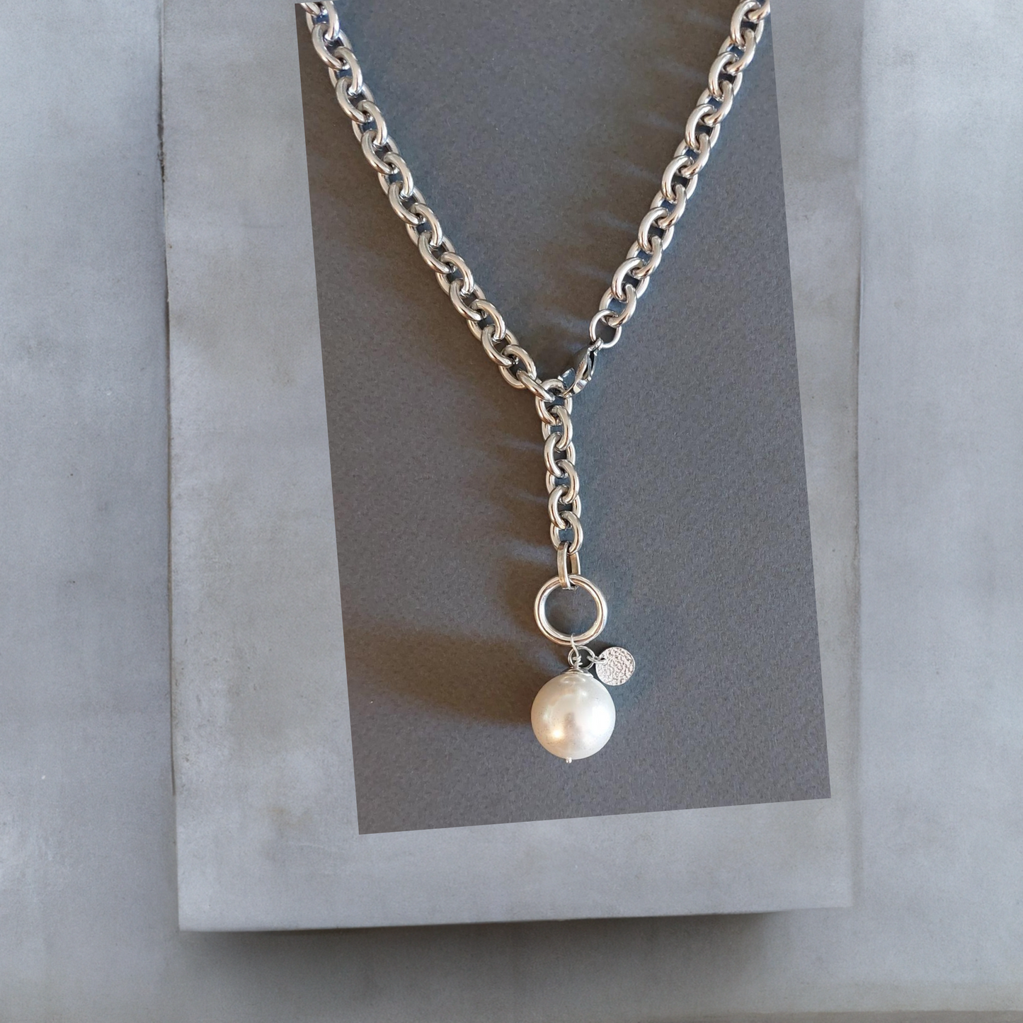 Breite Y-Halskette Lariatkette aus silberfarbenem Edelstahl mit einer großen weissen Mallorcaperle, die an einem silberfarbenen Ring befestigt ist. An der Mallorcaperle ist auch ein kleines gehämmertes Plättchen aus Sterlingsilber befestigt. Der Karabinerverschluss ist vorne flexibel zu schließen. Maximale Länge 50cm. Die Halskette ist von der Schmuckmarke Hug the Lioness aus Österreich und handgefertigt.