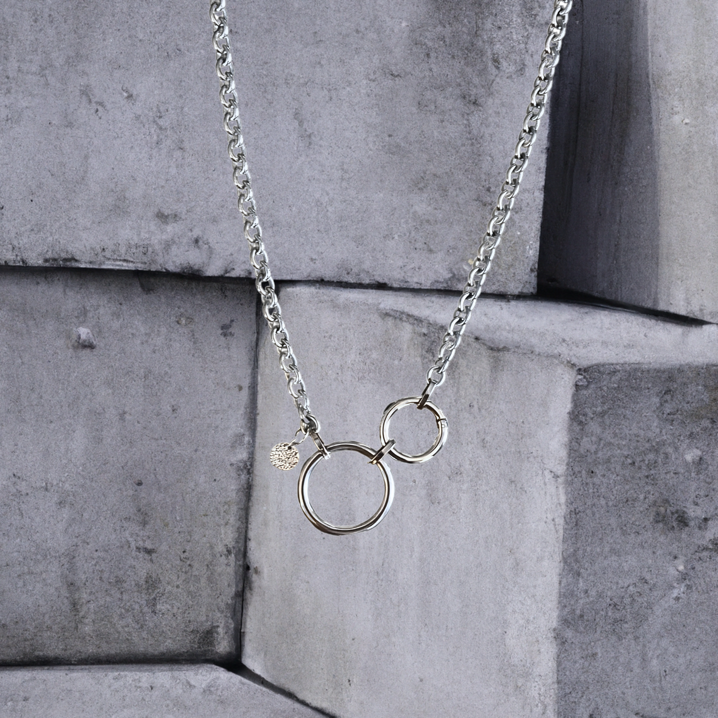 Statementkette von Hug the Lioness Silber und Edelstahlschmuck. 6mm breite silberfarbene Halskette 55cm aus Edelstahl mit einem 32mm großen Ring aus Edelstahl und einem 24mm Ringverschluss. Die Kette ist vorne mit dem Ringverschluss zu verschließen. Als Detail ist ein 10mm gehämmertes Plättchen aus Sterlingsilber angebracht.