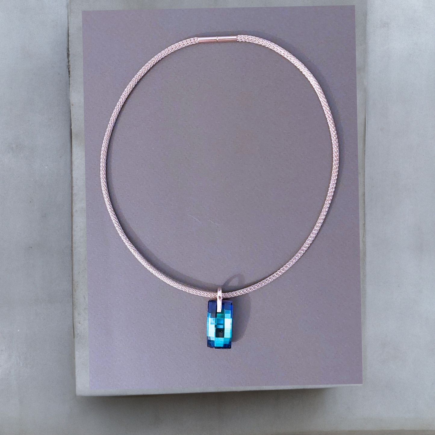 Silberfarbene Mesh Halskette aus Edelstahl mit einem großen rechteckigen blauen Kristallanhänger. Die moderne Meshkette ist 3mm breit und 45cm lang und stabil wie ein Halsreif. Der Kristall Urban ist 8mmx14mm in der Farbe Bermuda Blue. Der Kristall wurde in Österreich hergestellt. Die Kette hat einen Bajonettverschluss.