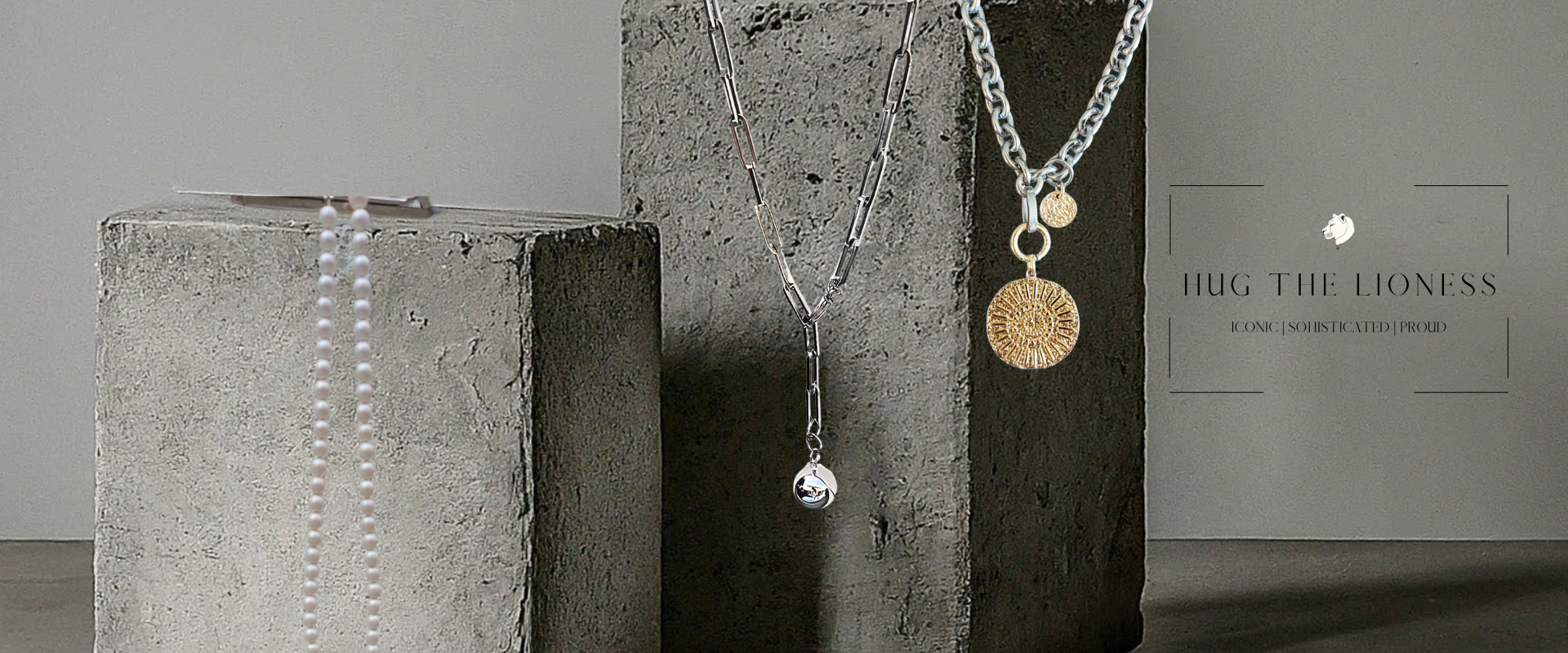 Banner Hug the Lioness Edelstahl Schmuck aus Österreich. Kette mit Anhänger Münze und y-Kette mit silberner Kugel. Auf grauen Betonblöcken.