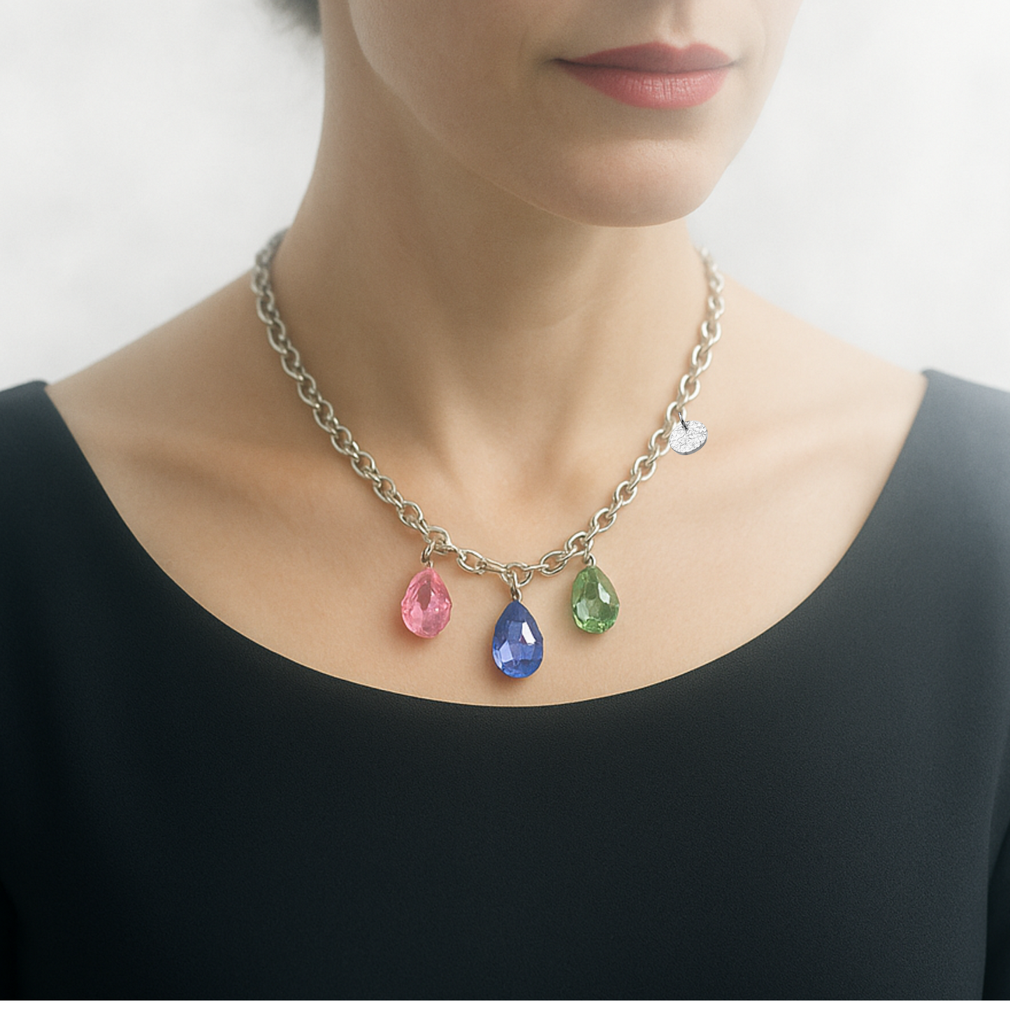 Collier aus Edelstahl, silberfarbene Gliederkette vorne mit 3 Kristalltropfen in rose, violett und grün. Die Kristalle sind aus Österreich. Die Kette ist 43cm lang und hat einen Karabinerverschluss. An der Seite ist in kleines gehämmertes Plättchen aus 925 Sterlingsilber angebracht. Die Kette ist aus der Kollektion JOY der Schmuckmarke HUG THE LIONESS.