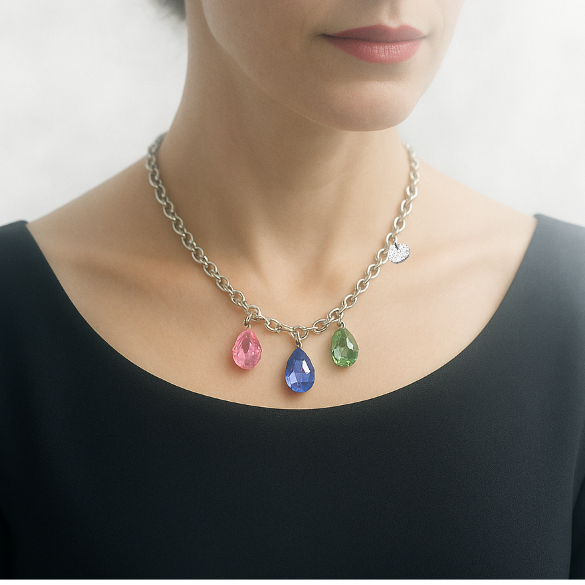 Collier aus Edelstahl, silberfarbene Gliederkette vorne mit 3 Kristalltropfen in rose, violett und grün. Die Kristalle sind aus Österreich. Die Kette ist 43cm lang und hat einen Karabinerverschluss. An der Seite ist in kleines gehämmertes Plättchen aus 925 Sterlingsilber angebracht. Die Kette ist aus der Kollektion JOY der Schmuckmarke HUG THE LIONESS.