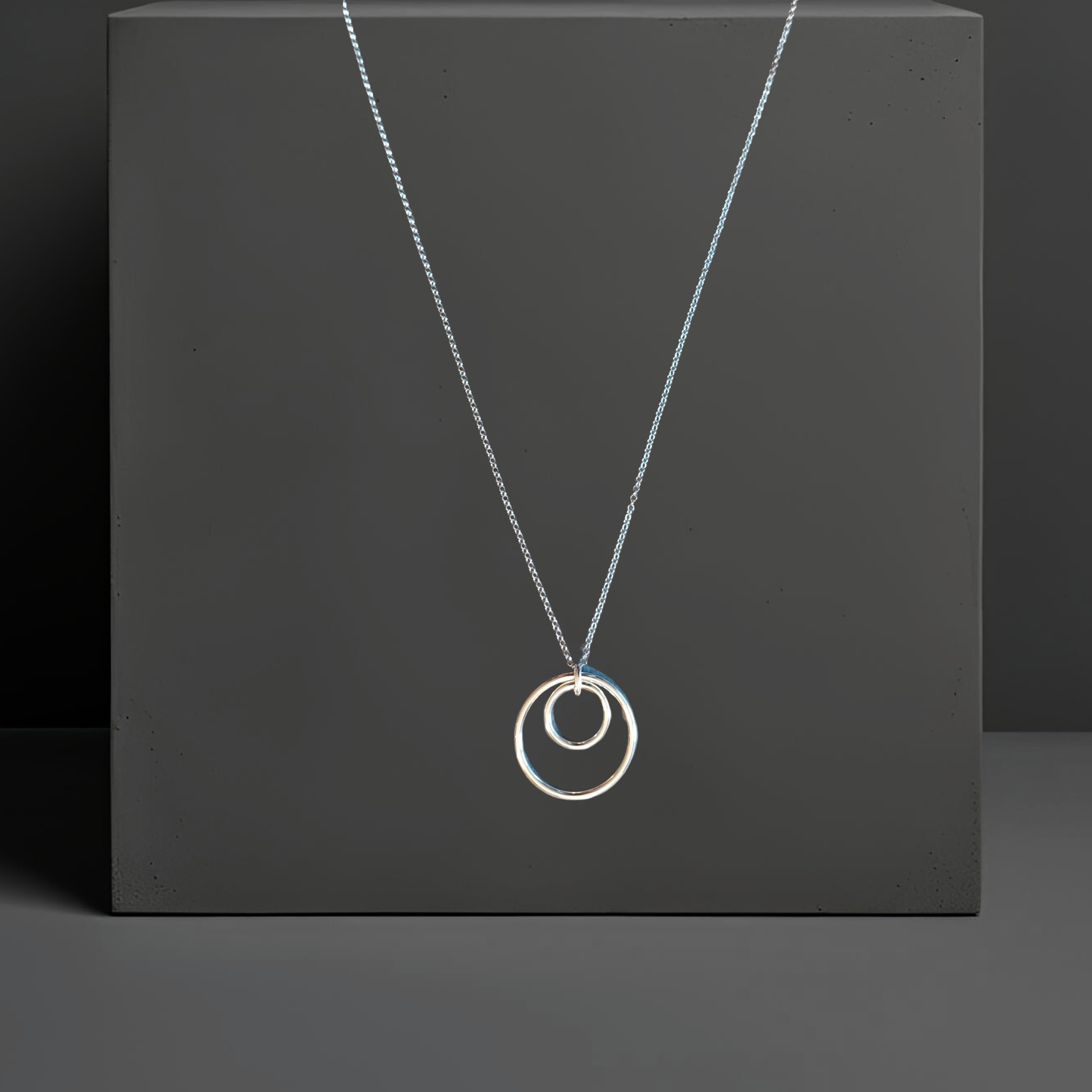 Feine 60cm Ankerkette in echt Silber. Der silberne Anhänger besteht aus zwei konzentrischen Ringen mit 16cm und 29cm. Die Kette hat einen Federringverschluss. Die Silberkette ist von der Schmuckmarke Hug the Lioness in Wattens, Österreich.