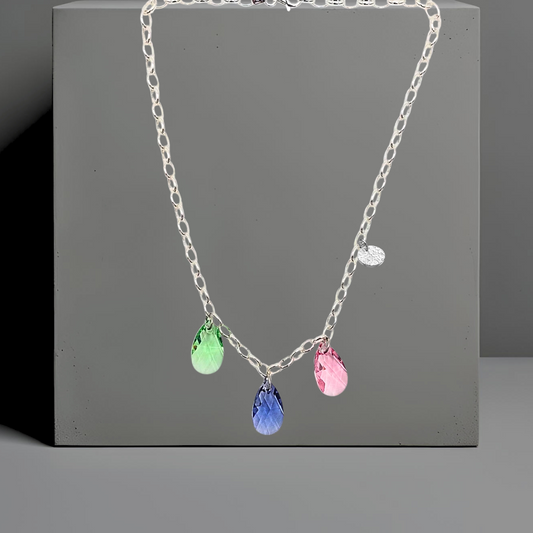 Collier aus 925 Sterlingsilber,  Gliederkette 5mm vorne mit 3 Kristalltropfen in rose, violett und grün. Die Kristalle sind aus Österreich. Die Kette ist 42cm lang und hat einen Karabinerverschluss. An der Seite ist in kleines gehämmertes Plättchen aus 925 Sterlingsilber angebracht. Die Kette ist aus der Kollektion JOY der Schmuckmarke HUG THE LIONESS.