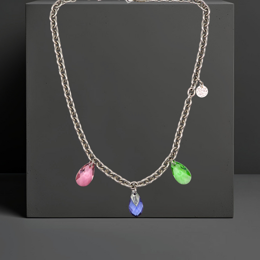 Collier aus Edelstahl, silberfarbene Gliederkette vorne mit 3 Kristalltropfen in rose, violett und grün. Die Kristalle sind aus Österreich. Die Kette ist 43cm lang und hat einen Karabinerverschluss. An der Seite ist in kleines gehämmertes Plättchen aus 925 Sterlingsilber angebracht. Die Kette ist aus der Kollektion JOY der Schmuckmarke HUG THE LIONESS.