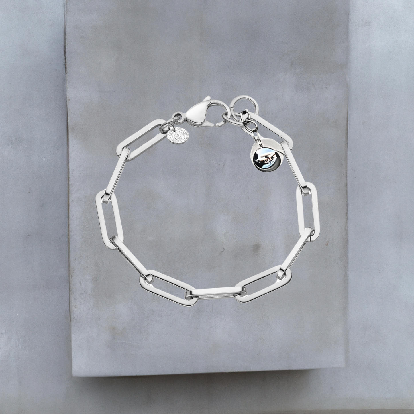 Exklusive Armkette von Hug the Lioness Schmuck. Silberfarbene Armkette aus glattem Edelstahl mit weiten Kettengliedern. An einem Ende der Armkette ist eine glänzende silberne Kugel aus Sterlingsilber angebracht. Neben dem großen Karabinerverschluss ist ein kleines gehämmertes Silberplättchen angebracht.