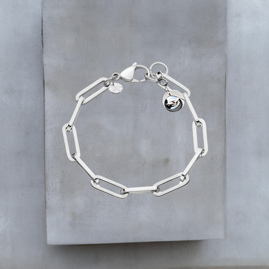 Exklusive Armkette von Hug the Lioness Schmuck. Silberfarbene Armkette aus glattem Edelstahl mit weiten Kettengliedern. An einem Ende der Armkette ist eine glänzende silberne Kugel aus Sterlingsilber angebracht. Neben dem großen Karabinerverschluss ist ein kleines gehämmertes Silberplättchen angebracht.