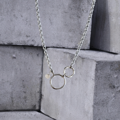 Statementkette von Hug the Lioness Silber und Edelstahlschmuck. 6mm breite silberfarbene Halskette 55cm aus Edelstahl mit einem 32mm großen Ring aus Edelstahl und einem 24mm Ringverschluss. Die Kette ist vorne mit dem Ringverschluss zu verschließen. Als Detail ist ein 10mm gehämmertes Plättchen aus Sterlingsilber angebracht.