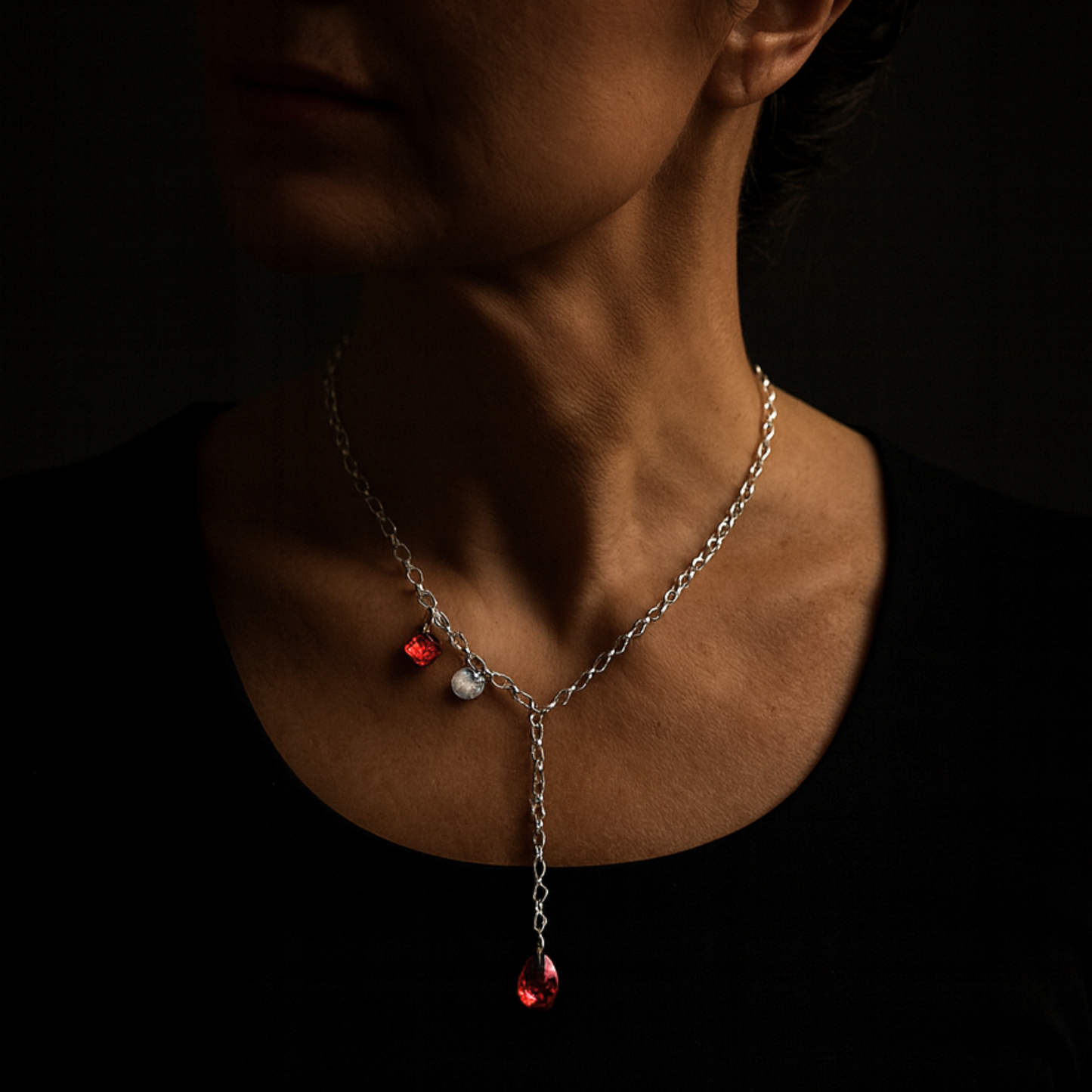Frau mit eleganter Y-Kette, Kristallkette mit 2 roten Kristallen aus 925 Sterlingsilber. Der Stil ist modern und elegant. Die Kette ist vorne zu schließen und die Länge ist variabel. Die Silberkette ist 50cm lang, am Ende ist ein roter Kristalltropfen angebracht, an der Seite ein viereckiger roter Kristall und ein gehämmertes Silberplättchen. Die Kette ist von der Schmuckmarke HUG THE LIONESS
