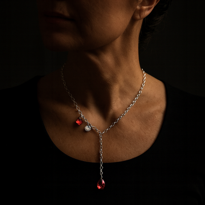 Frau mit eleganter Y-Kette, Kristallkette mit 2 roten Kristallen aus 925 Sterlingsilber. Der Stil ist modern und elegant. Die Kette ist vorne zu schließen und die Länge ist variabel. Die Silberkette ist 50cm lang, am Ende ist ein roter Kristalltropfen angebracht, an der Seite ein viereckiger roter Kristall und ein gehämmertes Silberplättchen. Die Kette ist von der Schmuckmarke HUG THE LIONESS