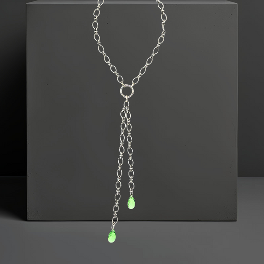 Handgefertigte breite Gliederkette aus rostfreiem Edelstahl mit einem Ringverschluss vorne. Im Ringverschluss ist ein langer Anhänger angebracht, der aus 2 Ketten (17cm und 25cm) und jeweils einem peridot grünem Kristalltropfen am Ende der Ketten besteht. Der lange Anhänger kann auch abgenommen werden und die Kette mit dem Ringverschluss als kurzes Collier getragen werden. Die Halskette ist von der Schmuckmarke Hug the Lioness aus Österreich.