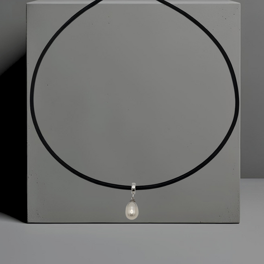 Schwarze 45cm Lederkette, rund, mit einer weißen Süsswasserperle als Anhänger. Die längliche Perle ist 9*11 mm gross und mit einem Anhängerring aus Silber an der Lederkette angebracht. Die Kette hat einen Karabinerverschluss. Der Hintergrund der Kette ist grau.