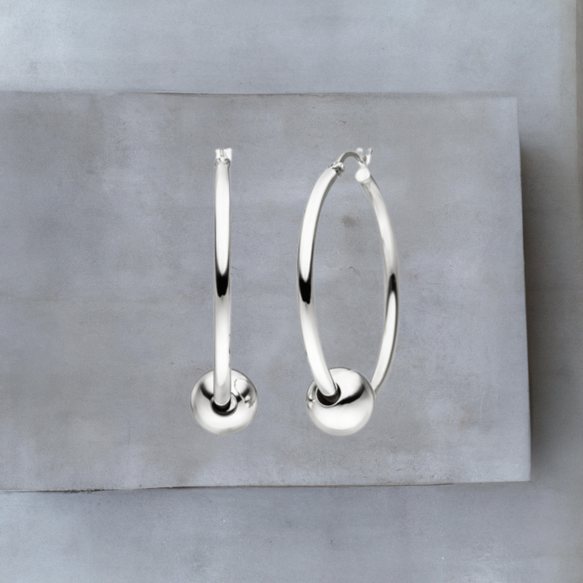 Ohrschmuck von Hug the Lioness.Die glatten Creolen aus Sterlingsilber haben einen Durchmesser von 36,5 mm und eine Stärke ca. 2,4 mm. Die Creolen sind jeweils durch eine glatte silberne Kugel von 10mm gezogen. Die Kugel befindet sich am unteren Teil der Creole. Die Creolen haben einen Hebelverschluss.
