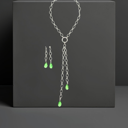 Handgefertigte breite Gliederkette aus rostfreiem Edelstahl mit einem Ringverschluss vorne. Die passenden Ohrhänger sind ebenfalls abgebildet. Im Ringverschluss der Kette ist ein langer Anhänger angebracht, der aus 2 Ketten (17cm und 25cm) und jeweils einem peridot grünem Kristalltropfen am Ende der Ketten besteht. Der lange Anhänger kann auch abgenommen werden und die Kette mit dem Ringverschluss als kurzes Collier getragen werden. Die Halskette ist von der Schmuckmarke Hug the Lioness aus Österreich. 