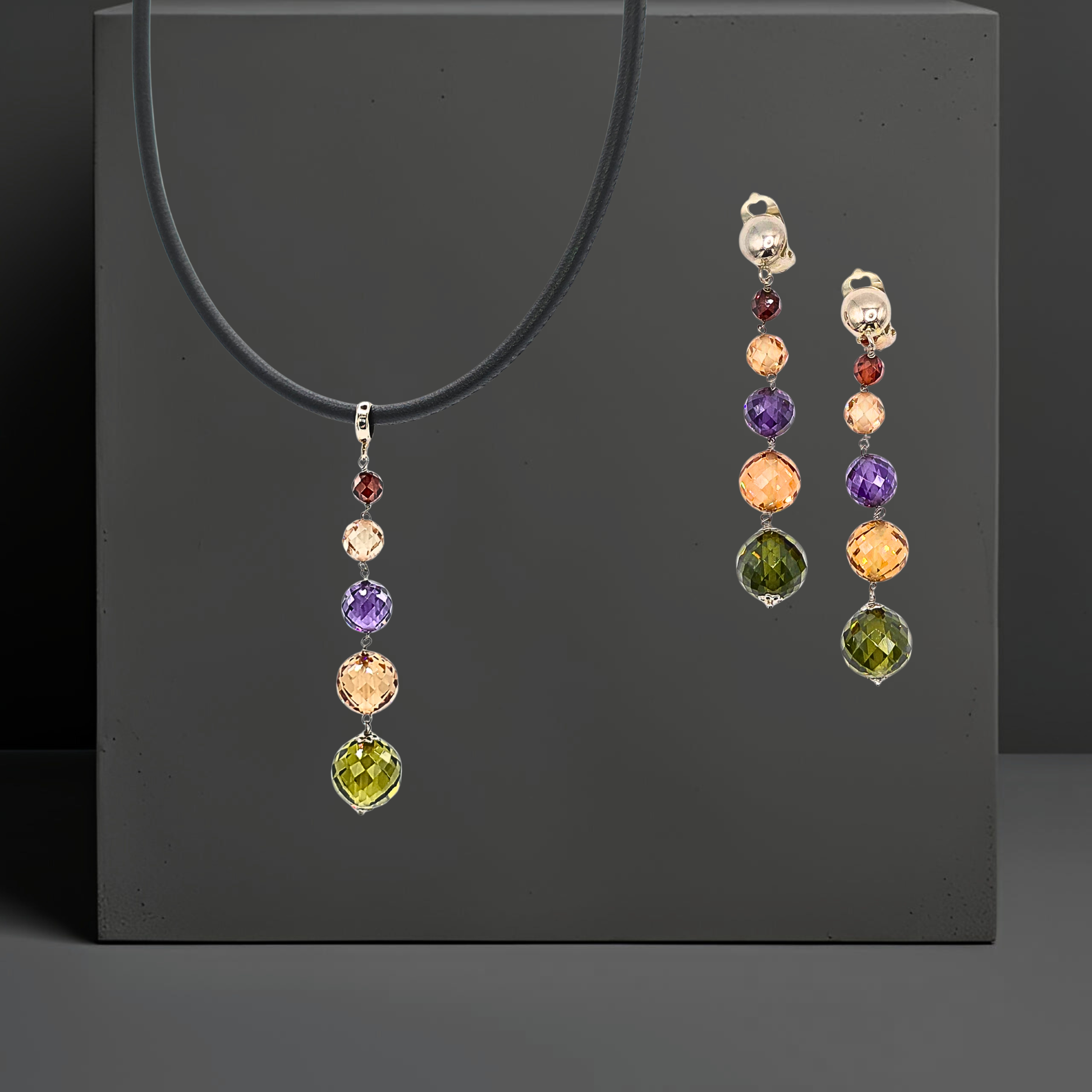 Set mit bunten Zirkonen handgefertigt:  Lederkette und Ohrclipsen mit Anhänger aus farbigen Zirkonen. Anhänger und Ohrringe sind 75mm lang und bestehen jeweils aus 5 leuchtenden, facettierten Zirkonkugeln in grün, goldgelb, violett, rose und rot    in abgestufter Größe. Der Schmuck ist von der Marke Hug the Lioness.