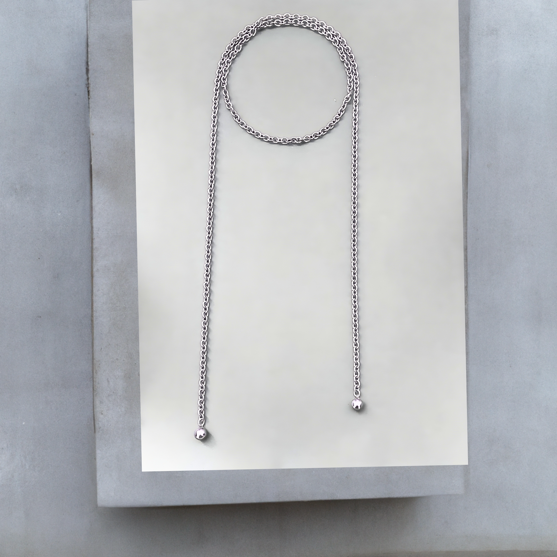 Lange Wickelkette oder Lassokette  aus silbernem Edelstahl. Die moderne Wickelkette ist 120mm lang und 6mm breit und wird einmal um den Hals geschlungen, die langen Enden hängen lose. An jedem Ende der Halskette ist eine 16mm silbergraue Mallorcaperle angebracht. Die Kette hat keinen Verschluss. Das stylishe Schmuckstück ist von der Schmuckmarke Hug the Lioness aus Österreich. 