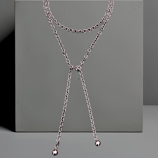Lange Wickelkette oder Lassokette  aus silbernem Edelstahl. Die moderne Wickelkette ist 120mm lang und 6mm breit und wird einmal um den Hals geschlungen, die langen Enden hängen lose. An jedem Ende der Halskette ist eine 16mm silbergraue Mallorcaperle angebracht. Die Kette hat keinen Verschluss. Das stylishe Schmuckstück ist von der Schmuckmarke Hug the Lioness aus Österreich. 