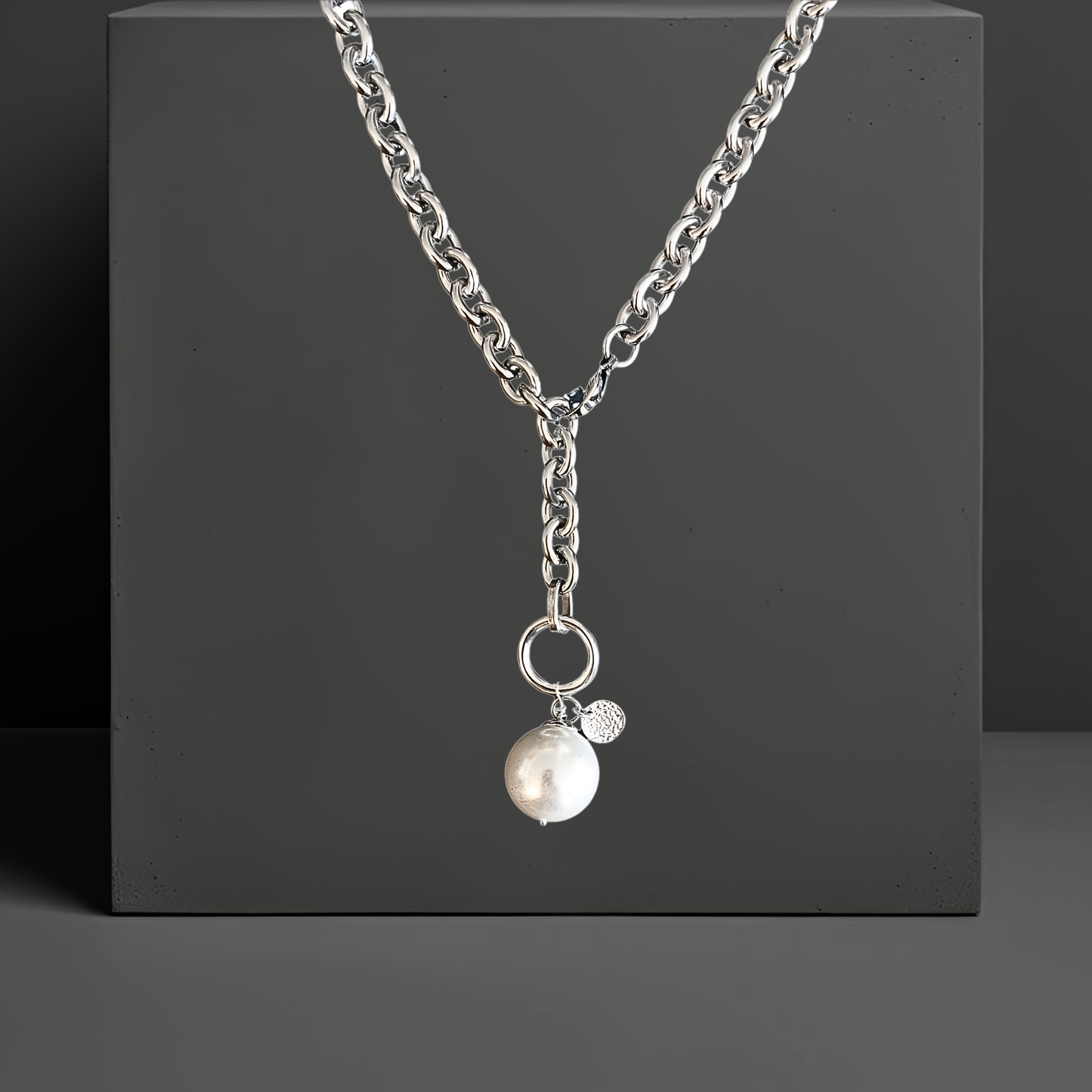 Moderne breite Y-Halskette Lariatkette aus silberfarbenem Edelstahl mit einer großen weissen Mallorcaperle, die an einem silberfarbenen Ring befestigt ist. Der Karabinerverschluss ist vorne flexibel zu schließen. Maximale Länge 50cm. An der Mallorcaperle ist auch ein kleines gehämmertes Plättchen aus Sterlingsilber befestigt. Die exklusive Halskette ist von der Schmuckmarke Hug the Lioness aus Wattens, Österreich und handgefertigt.